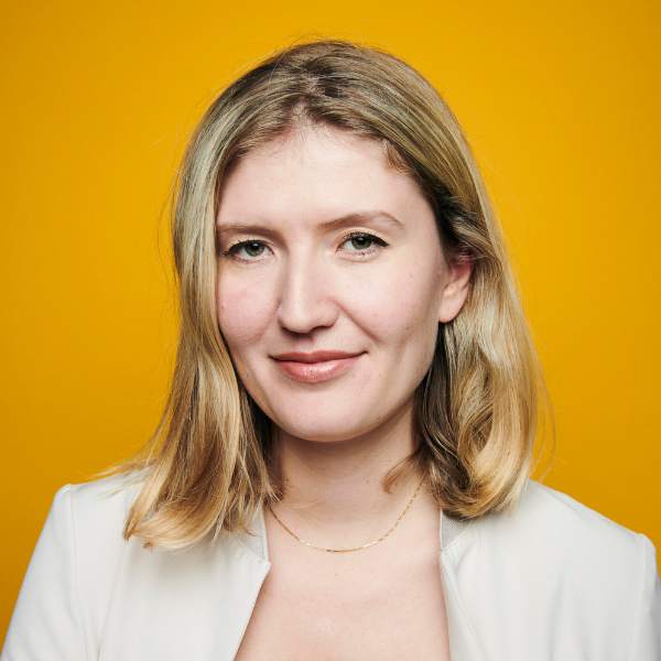 Headshot of Laura Ingram in a white jacket with a yellow background.